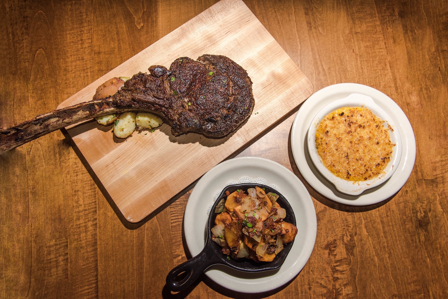 Steak on a cutting board with other side dishes in skillets.