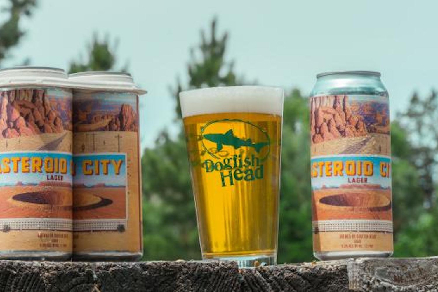 a four pack and glass of Dogfish Head Asteroid City Lager on a fence outside