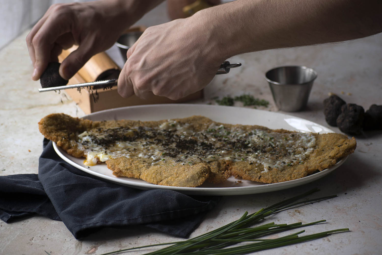 man grating cheese on top of veal.