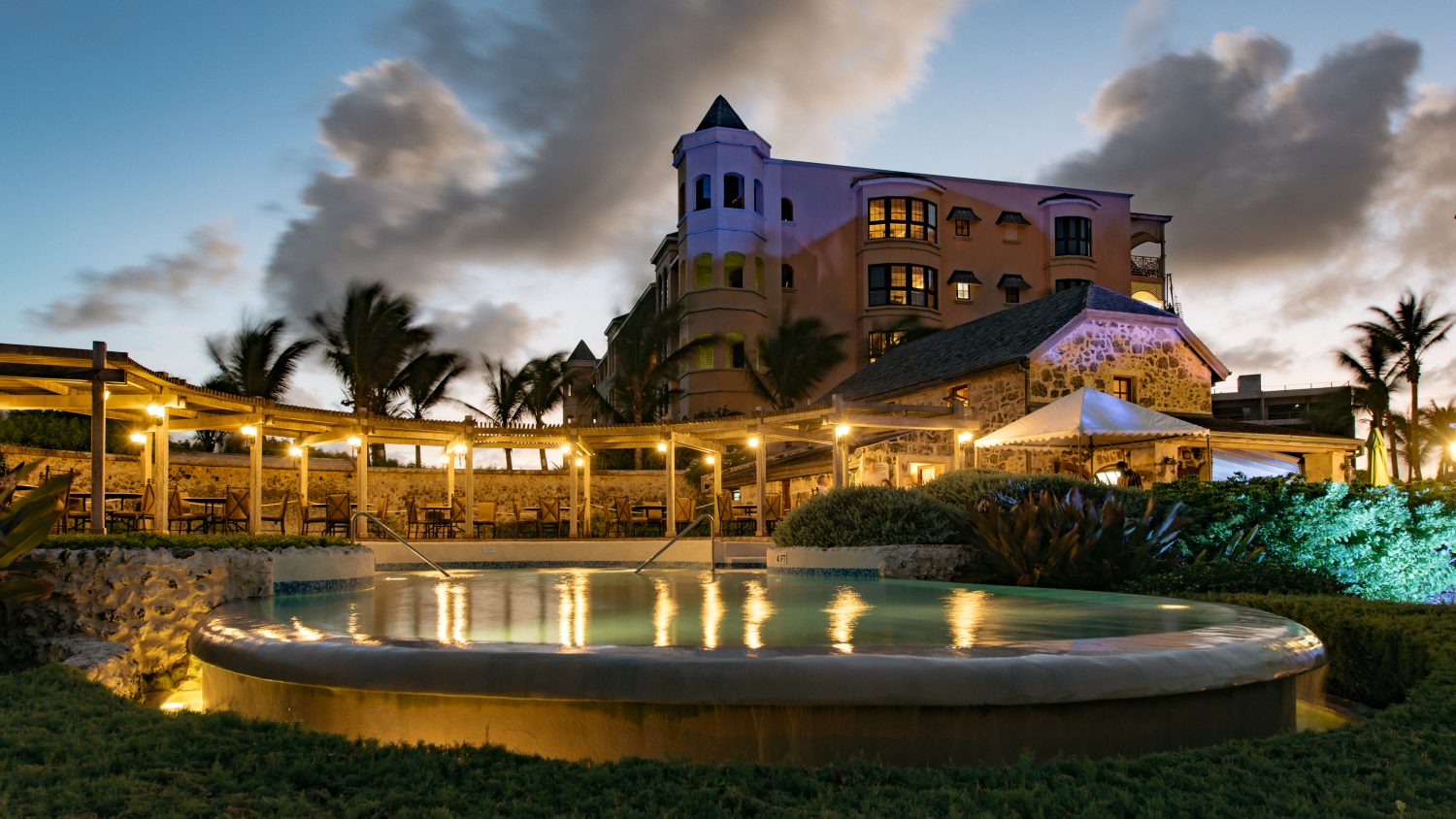 Pool at nighttime with candle lights in front of castle-like building.