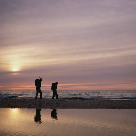 A father and a son walking next to a lake.