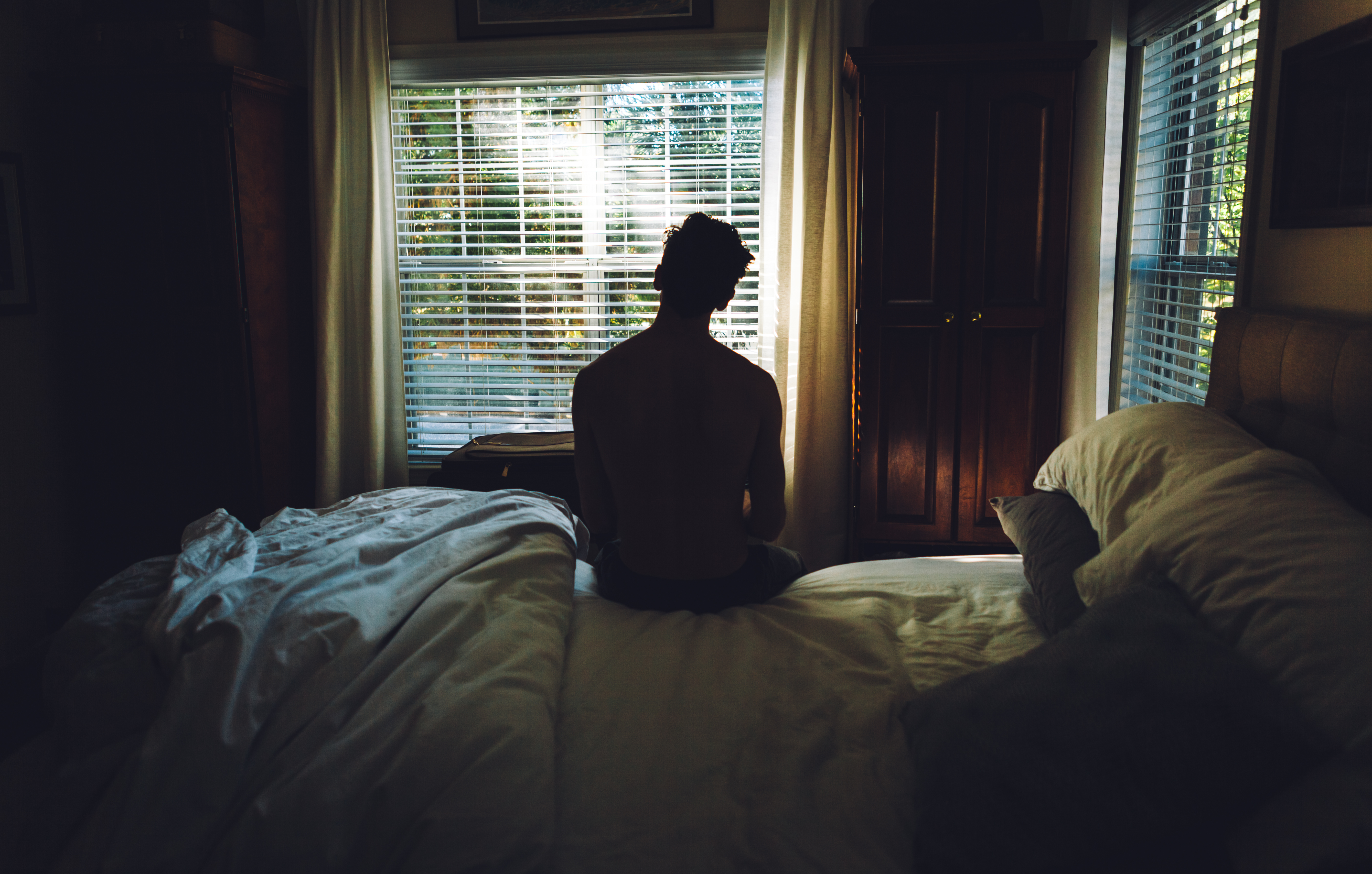 A man sitting on his bed staring out the window.
