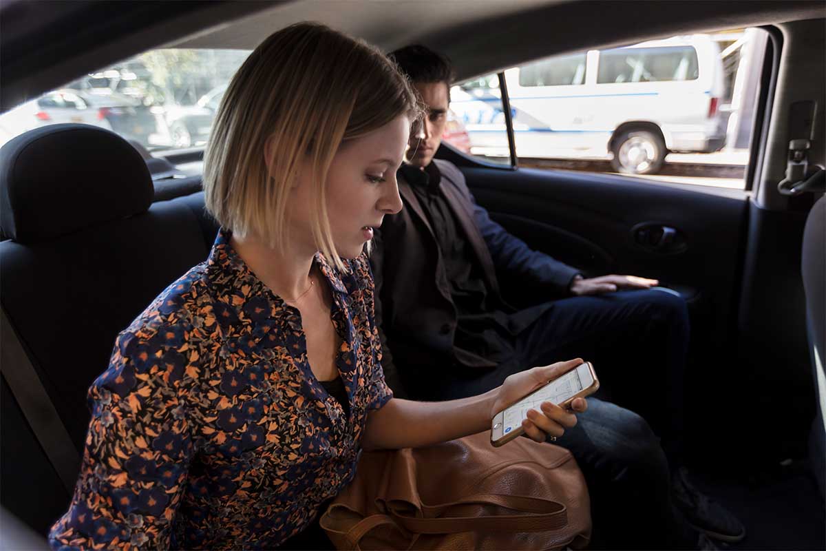 Man and woman sitting in car looking at phone. Uber has announced video ads are coming to its apps and even on tablets in its cars.