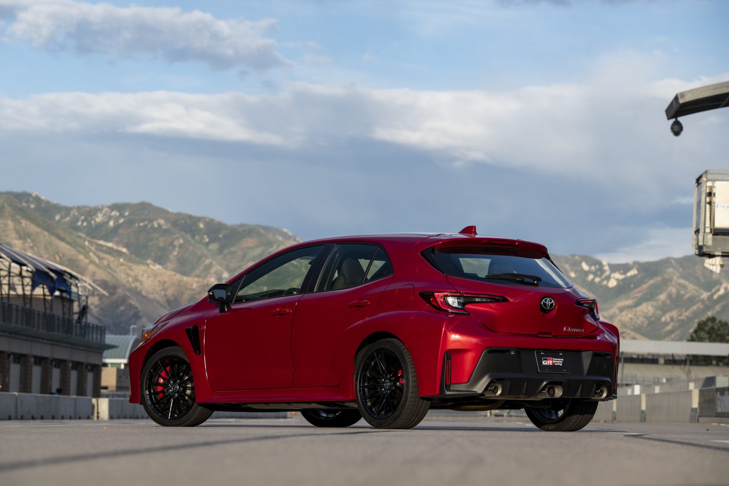A supersonic red-colored 2023 GR Corolla hatchback by Toyota sits on a paved road with mountains in the distance