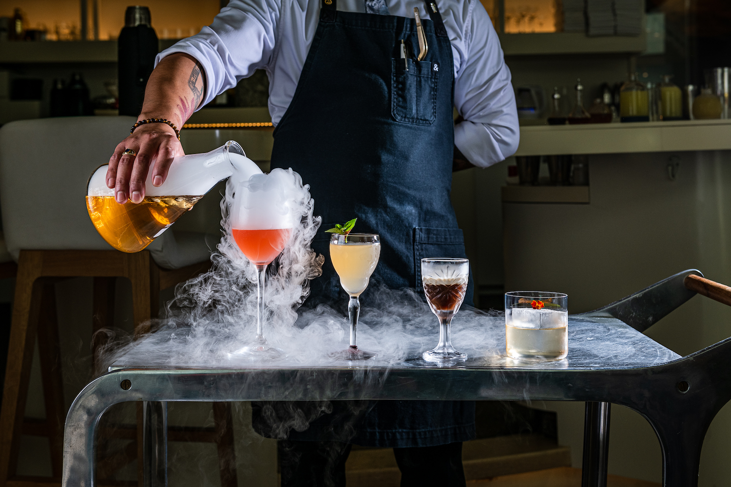 Four cocktails on a tray. Smoke is coming off of the tray from a bottle.