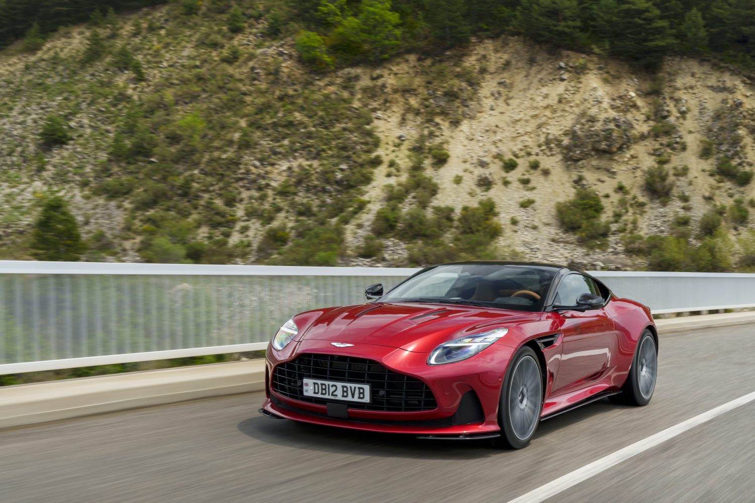 The Aston Martin DB12 speeds along a freeway next to a mountainside
