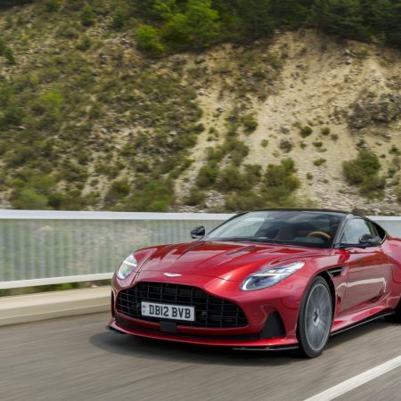 The Aston Martin DB12 speeds along a freeway next to a mountainside