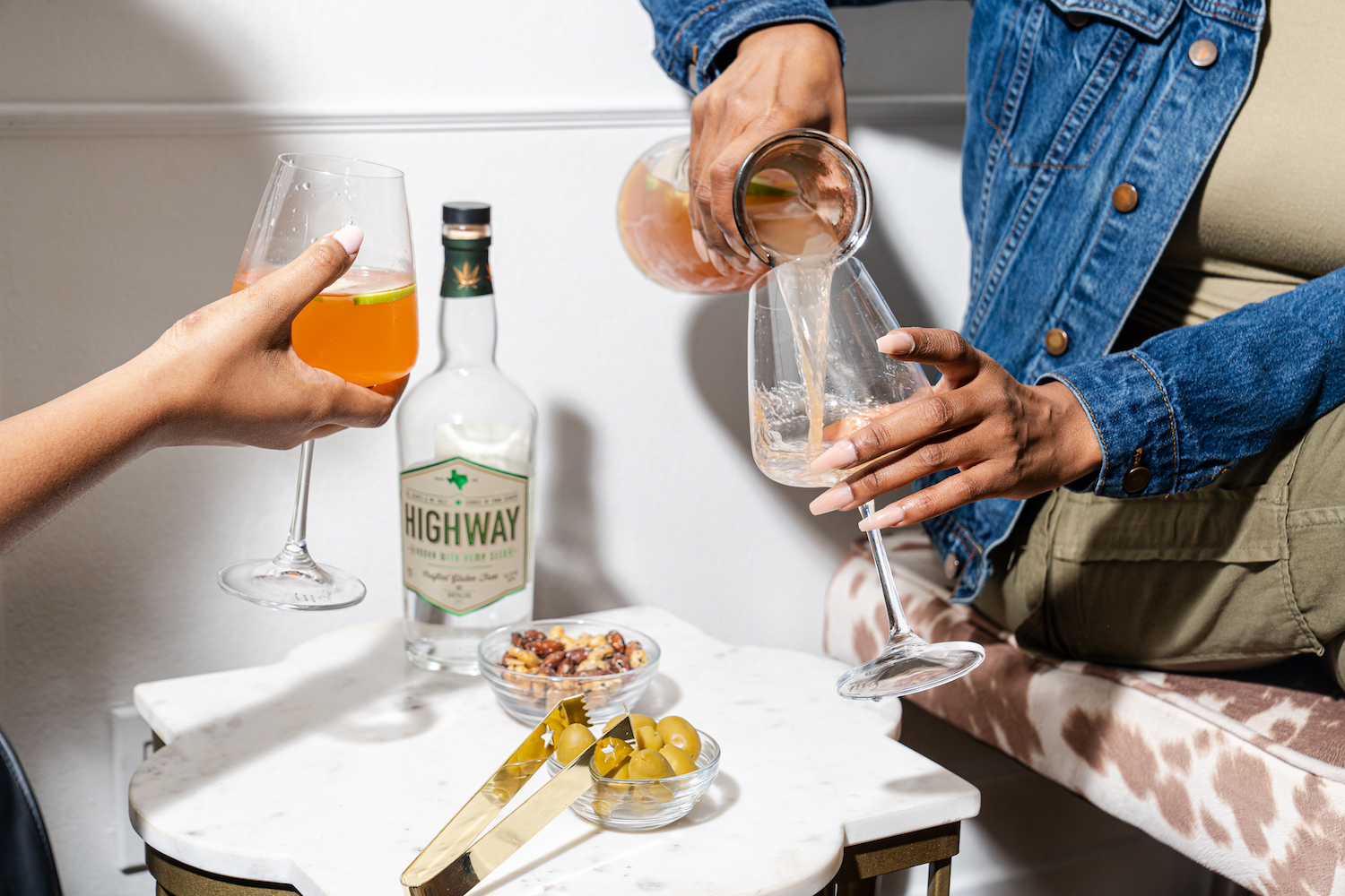 two hands holding wine glasses and pouring vodka-based cocktails into them.