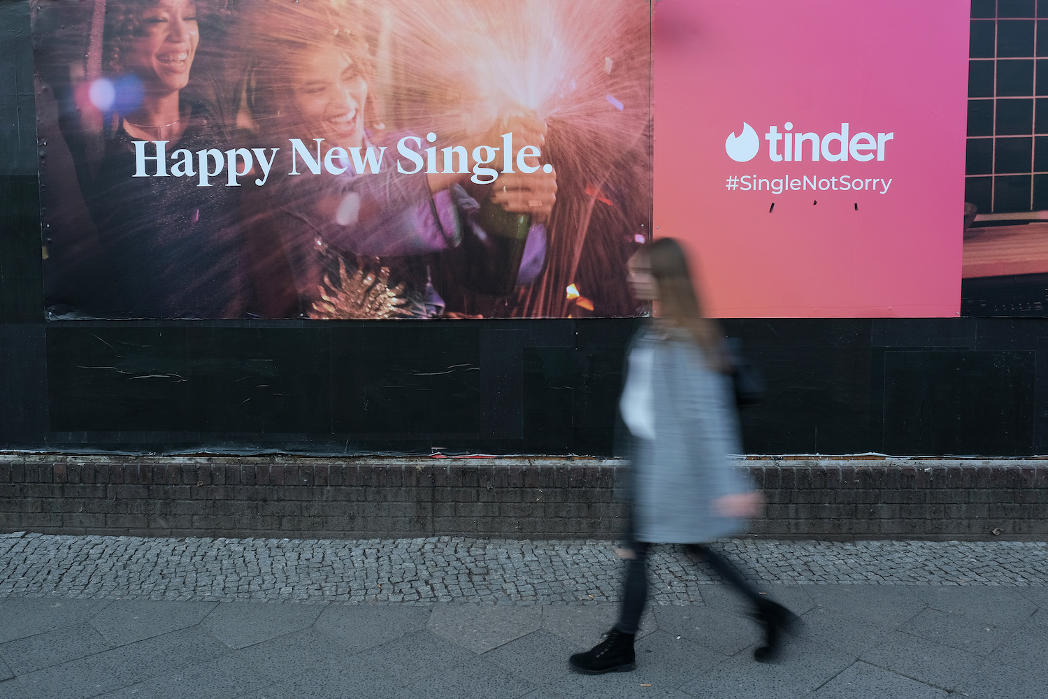 A young woman walks past a billboard advertisement for the dating app Tinder