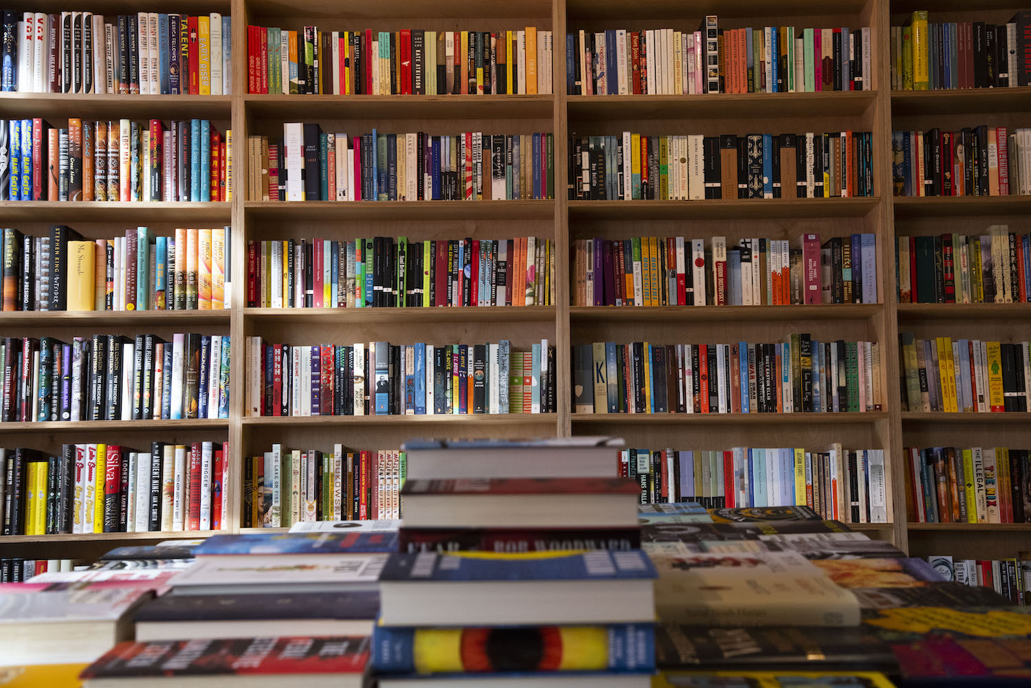 Books in a bookshelf behind a table of stacked books.