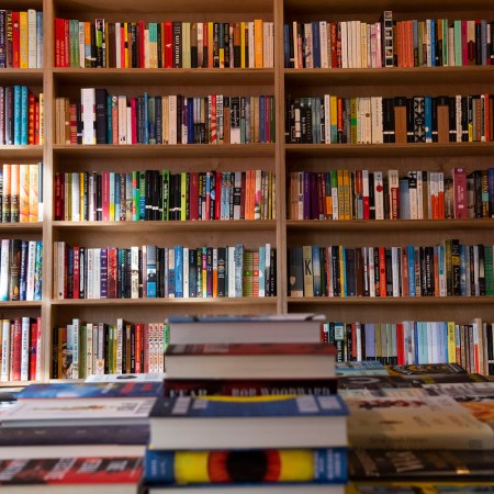 Books in a bookshelf behind a table of stacked books.