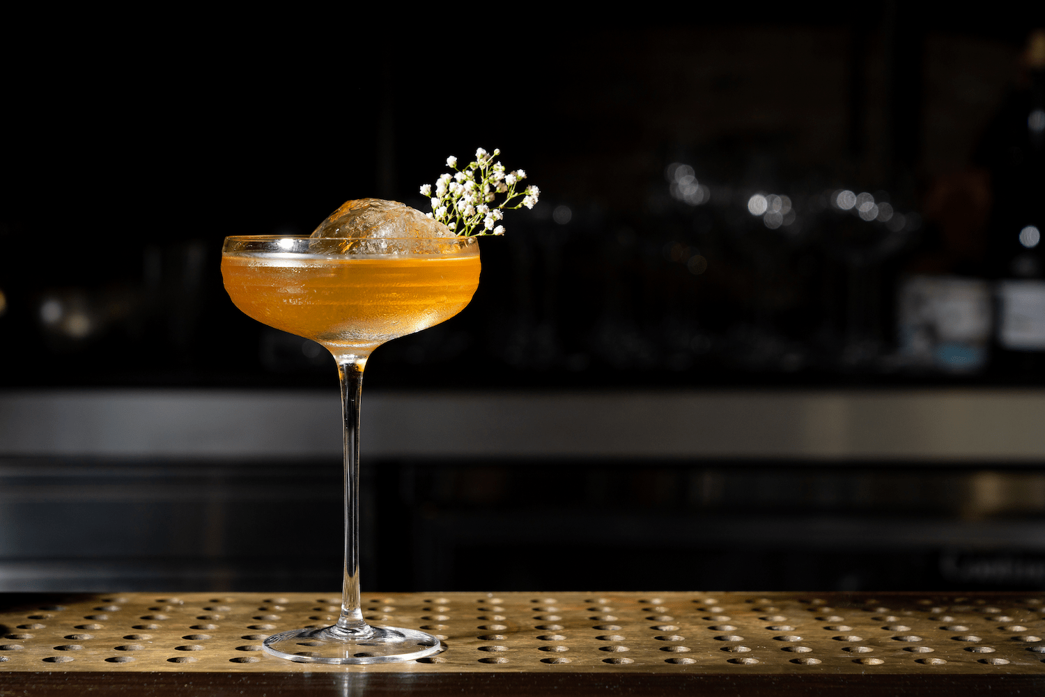 Fancy cocktail with sphere ice and herb spring on a bar counter.