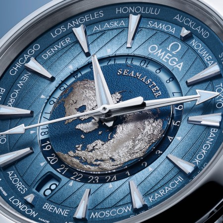 Up-close shot of a watch face that's blue with silver outlines of continents against a darker blue sphere, resembling Earth.