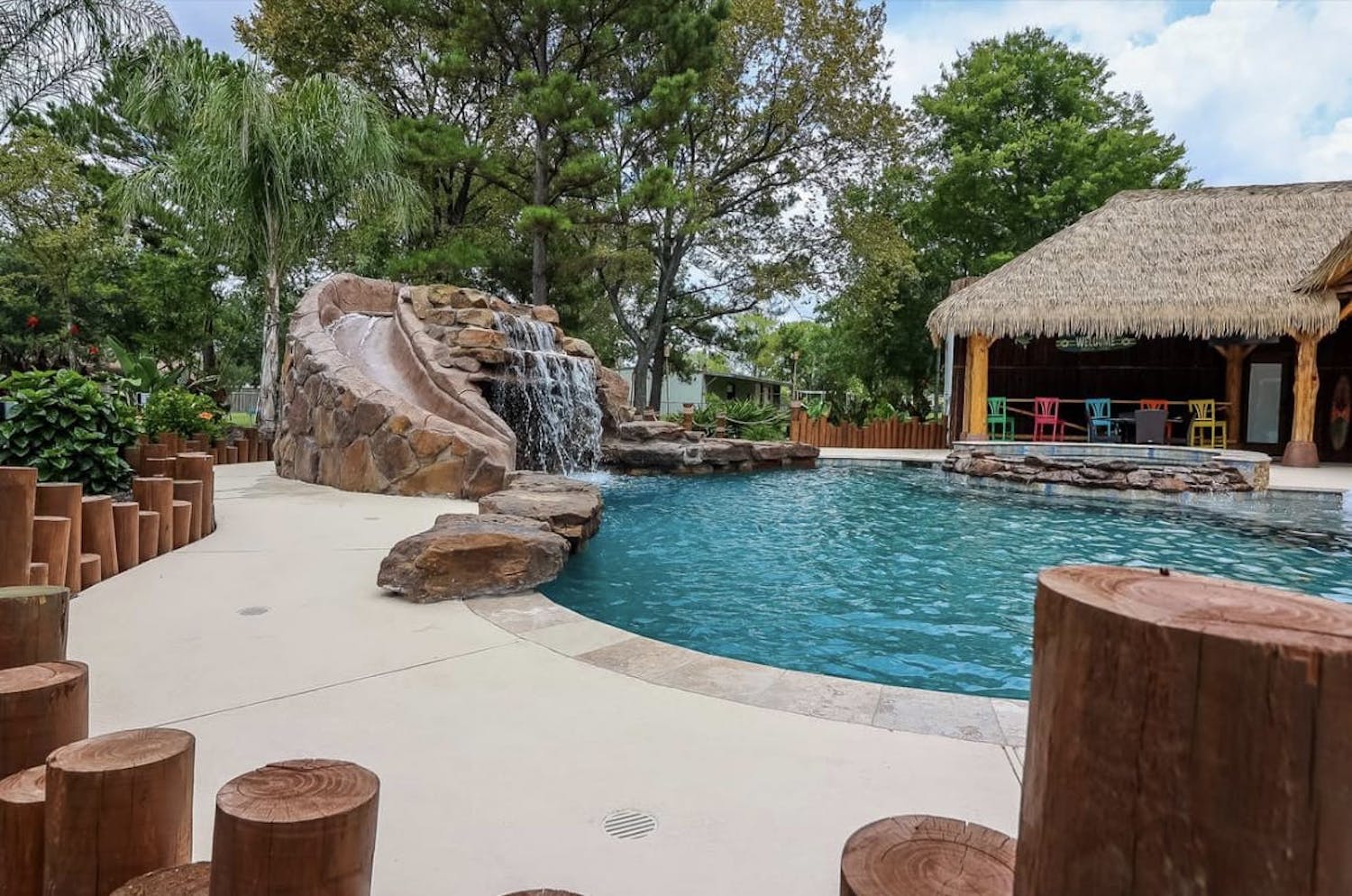 Tropical cabana with colorful chairs next to a pool with a waterslide and a waterfall.