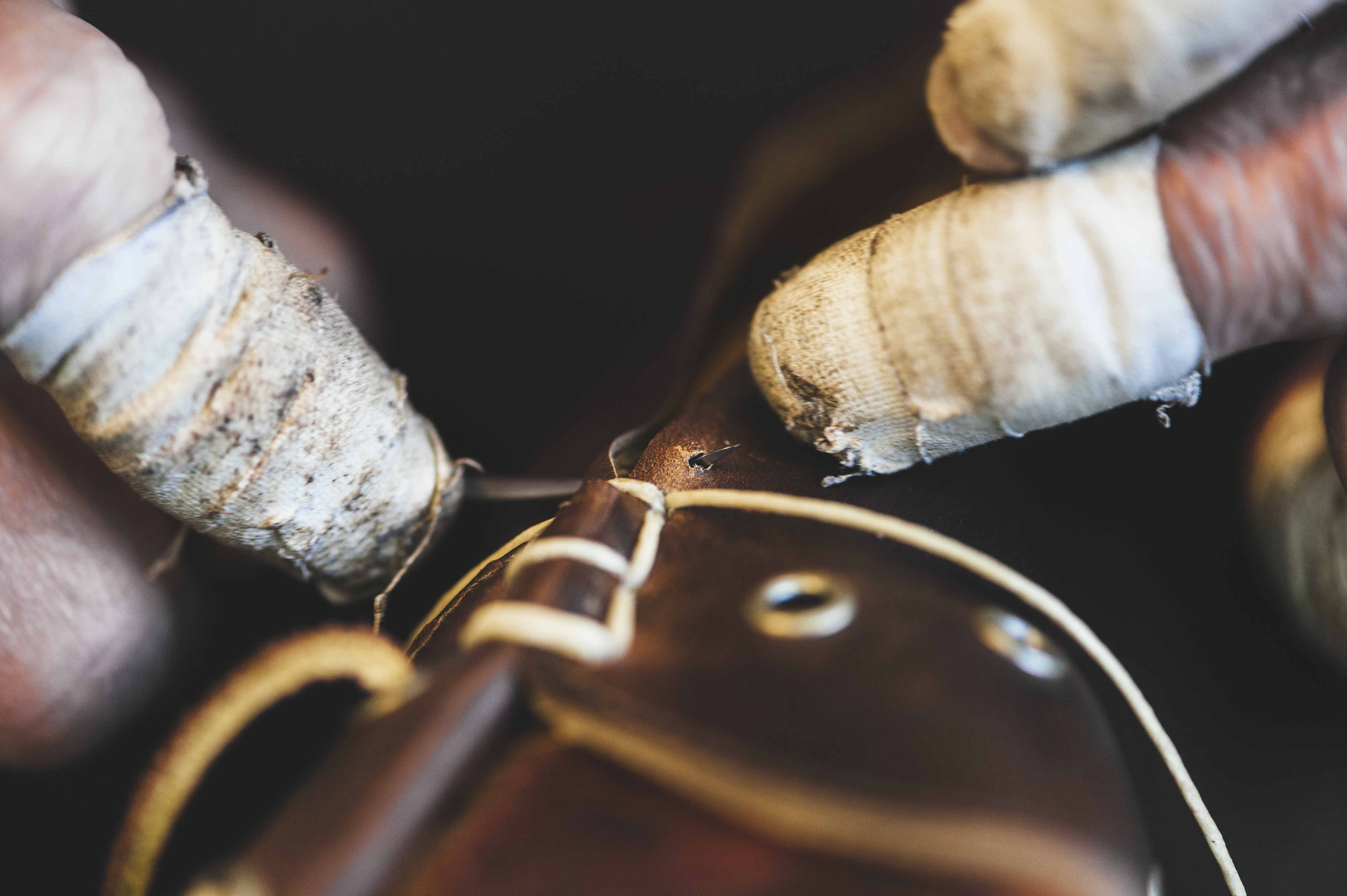 A worker wields a sharp, needle-like tool called an awl to slice holes into the hide.