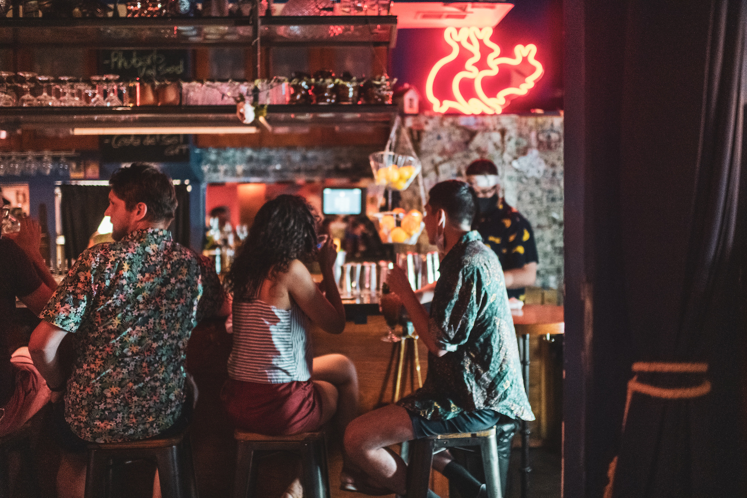 People sitting at a bar below neon signs.