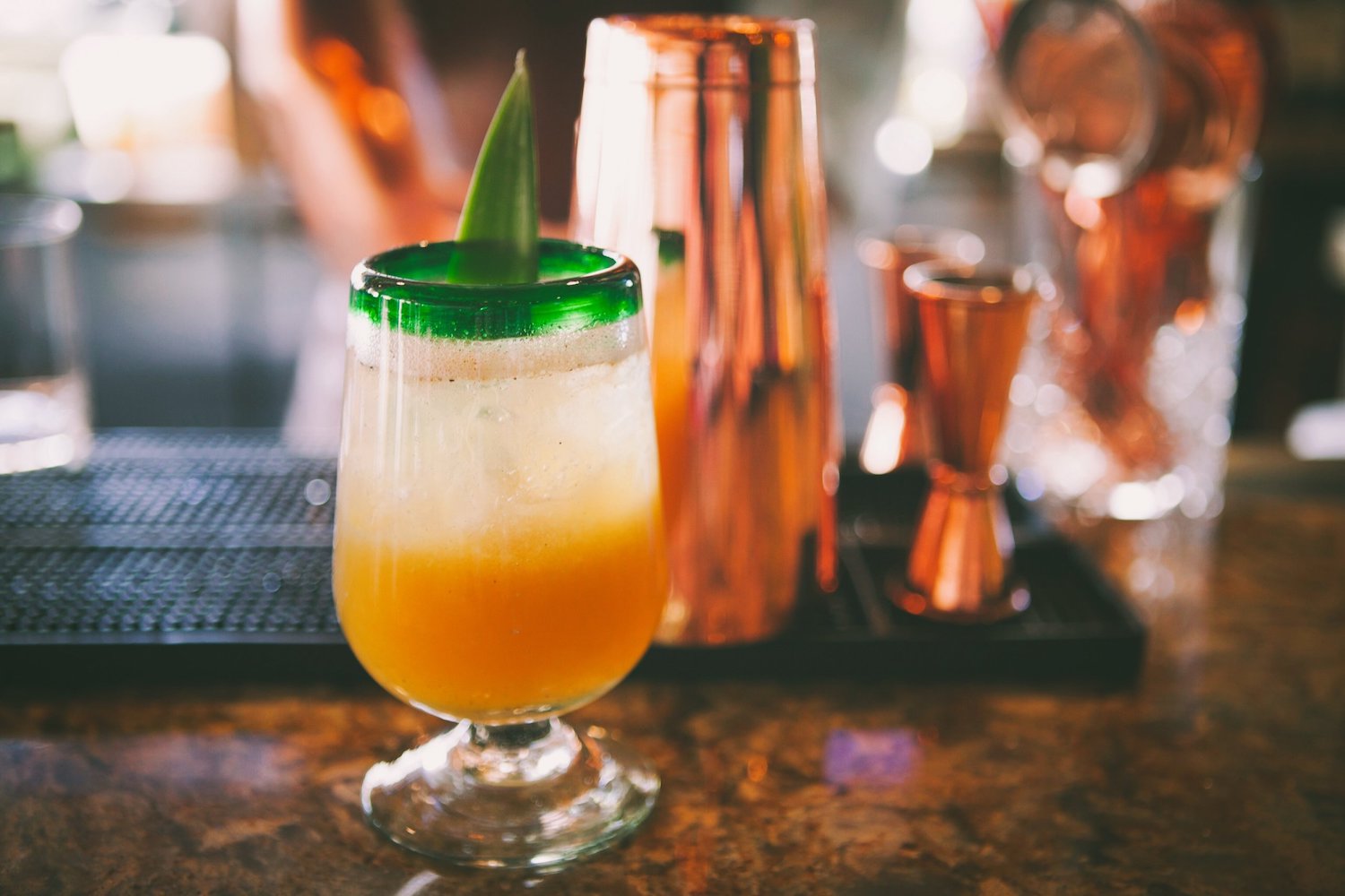 a tequila cocktail in a green rimmed footed glass with a pineapple leaf garnish