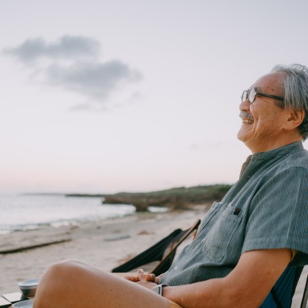 An old man sitting on the beach and smiling.