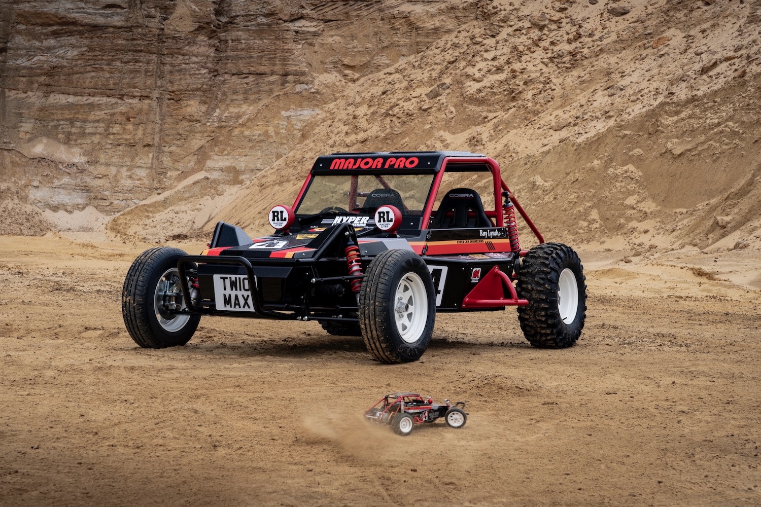 A red buggy vehicle in desert area next to the red toy car it's modeled after.