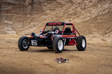 A red buggy vehicle in desert area next to the red toy car it's modeled after.