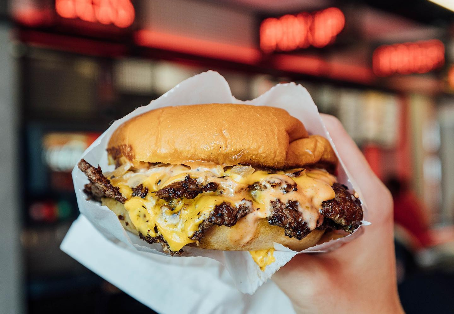 Burger with a lot of cheese being held in wrapper