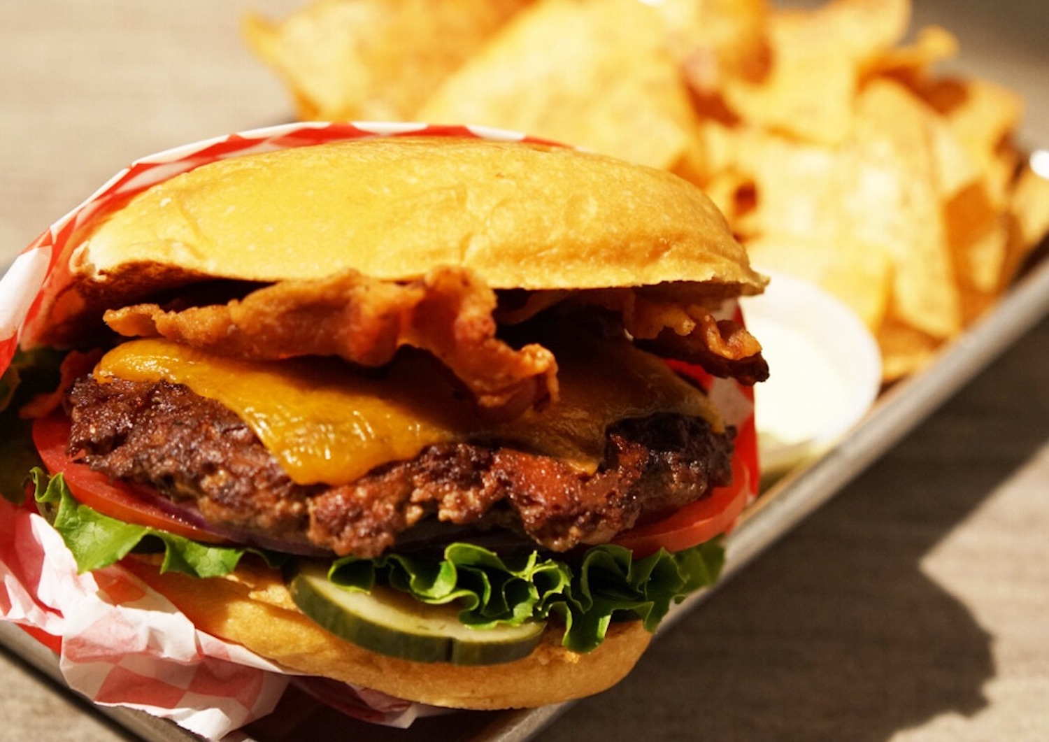 Burger in a red and white plastic wrap on a tray with chips