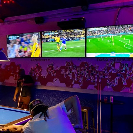 three screens TV in purple-ish lighting at bar
