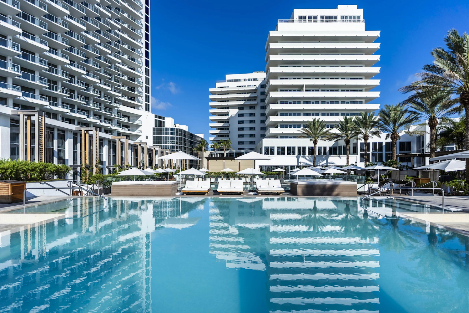 Pool area outside of a hotel with lounge chairs and palm trees.