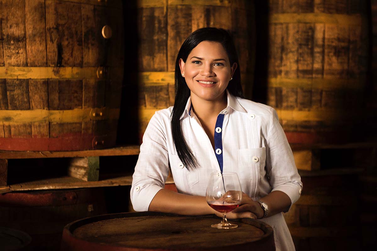 Brugal Master Distiller Jassil Villanueva Quintana with a glass of rum and behind some rum barrels