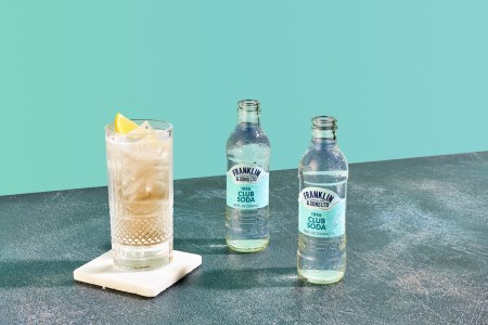 a whiskey highball next to Franklin & Sons club soda with a blue wall behind it