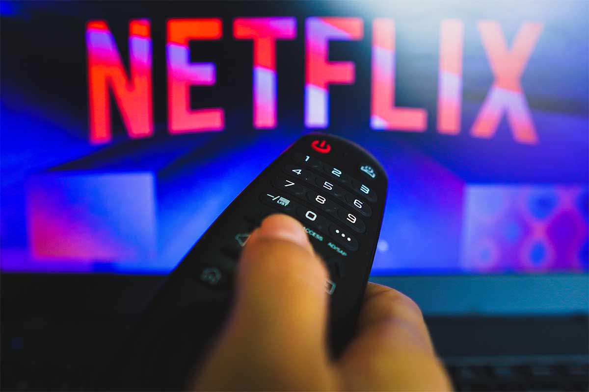 In this photo illustration, a hand holding a TV remote control in front of the Netflix logo on a TV screen.