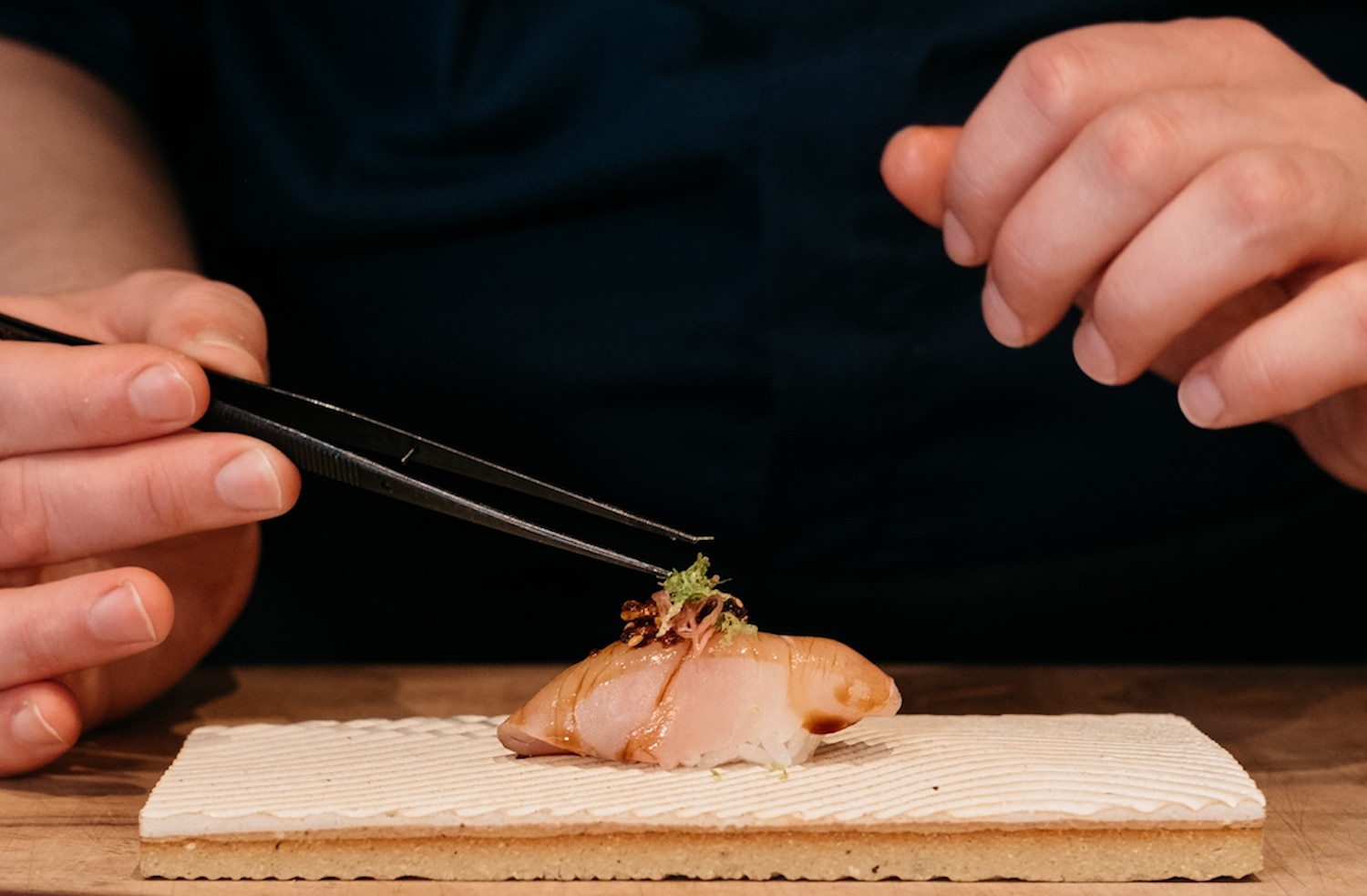 Sushi on a board about to be picked up by chopsticks