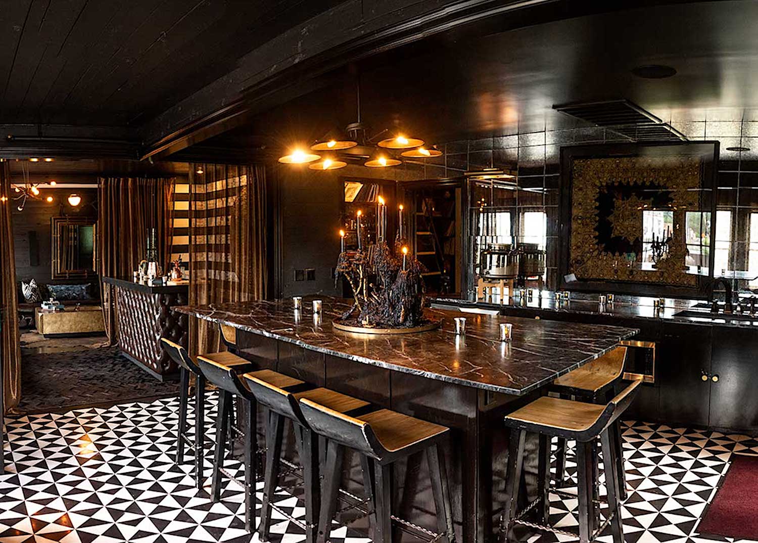 Large table in a dimly lit room with dark marble with black chandelier centerpiece and gold accents