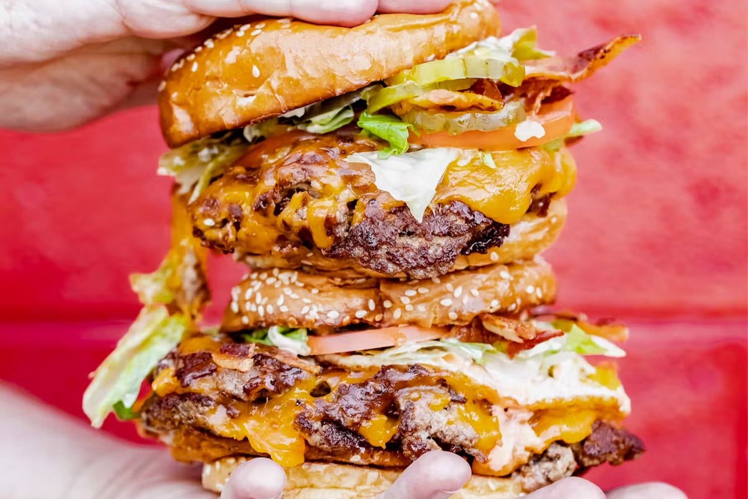 Two burgers being held against a red background