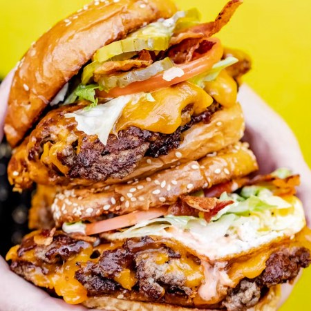 Two burgers being held in front of a yellow wall