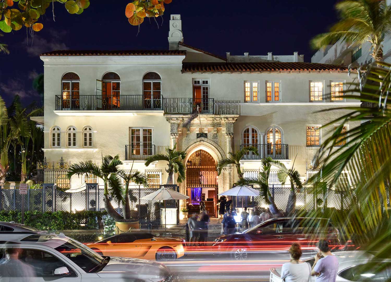 Cream-colored building with large windows at night with cars driving in front of it.