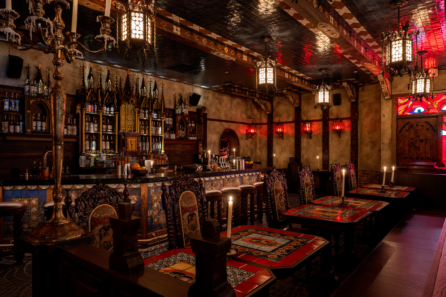 Chairs and tables with large candles in front of a bar, all designed to match interior of an old chapel.