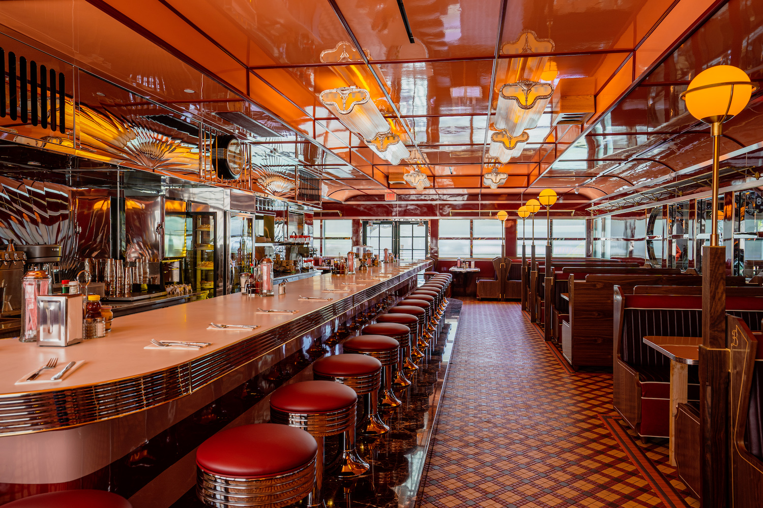 Red booths and bar stools in front of a bar at vintage-looking diner