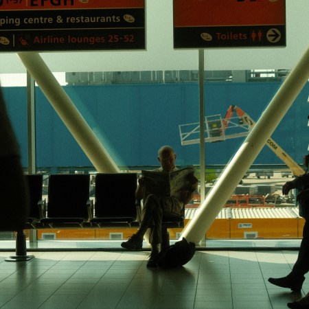 A man sitting cross-legged at the airport gate, reading a newspaper.