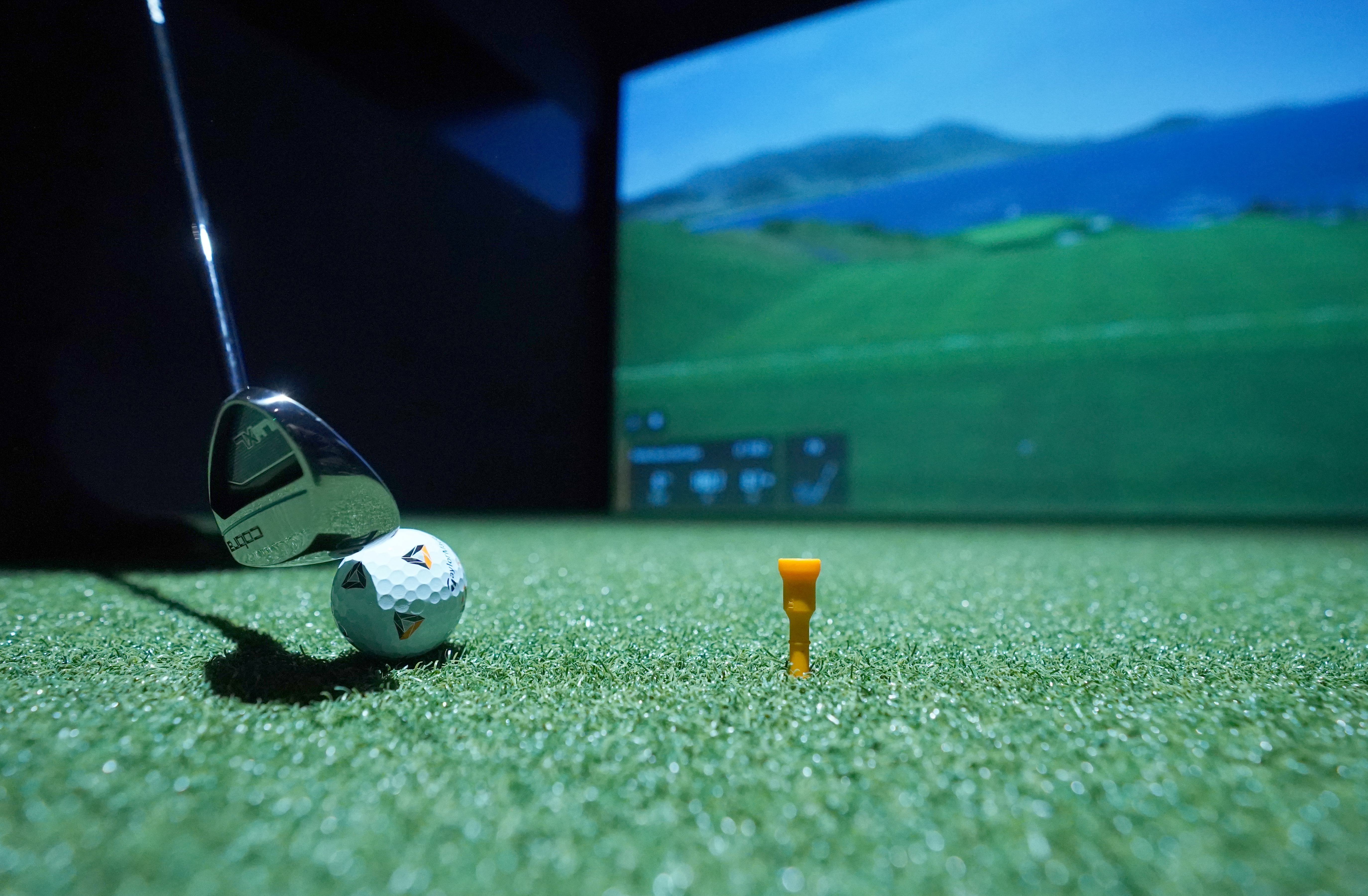 A golf club lining up a ball at an indoor golf simulator.