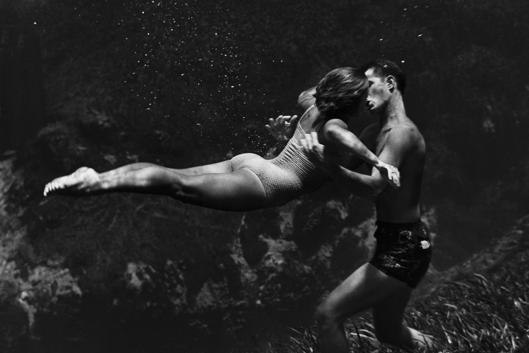 a black and white photo of a man and woman kissing under water