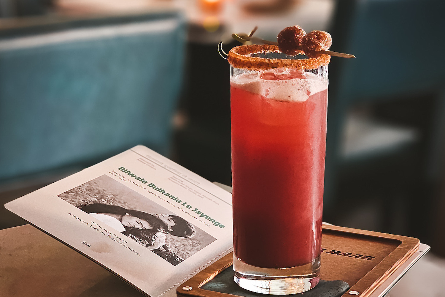 a red cocktail in a collins glass with a spicy salt rim and tamarind garnish