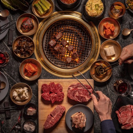 Steak being cooked over an open flame with spices and sides, Korean barbecue-style