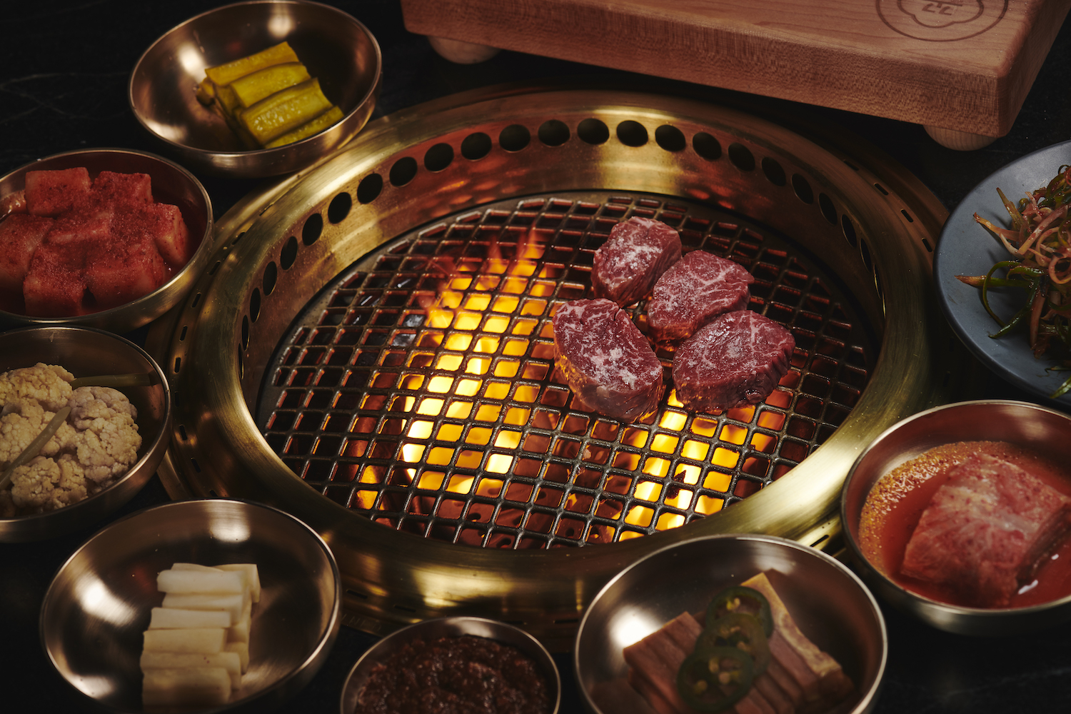 Steak being cooked over a flame with varieties of spices and sides