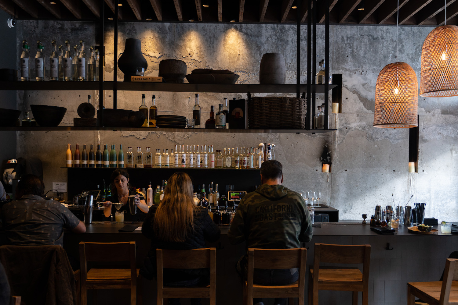 People sitting at bar area with bottles on shelves