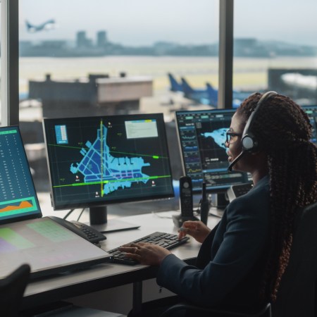 Female Air Traffic Controller with Headset Talk on a Call in Airport Tower. Office Room is Full of Desktop Computer Displays with Navigation Screens, Airplane Flight Radar Data for the Team