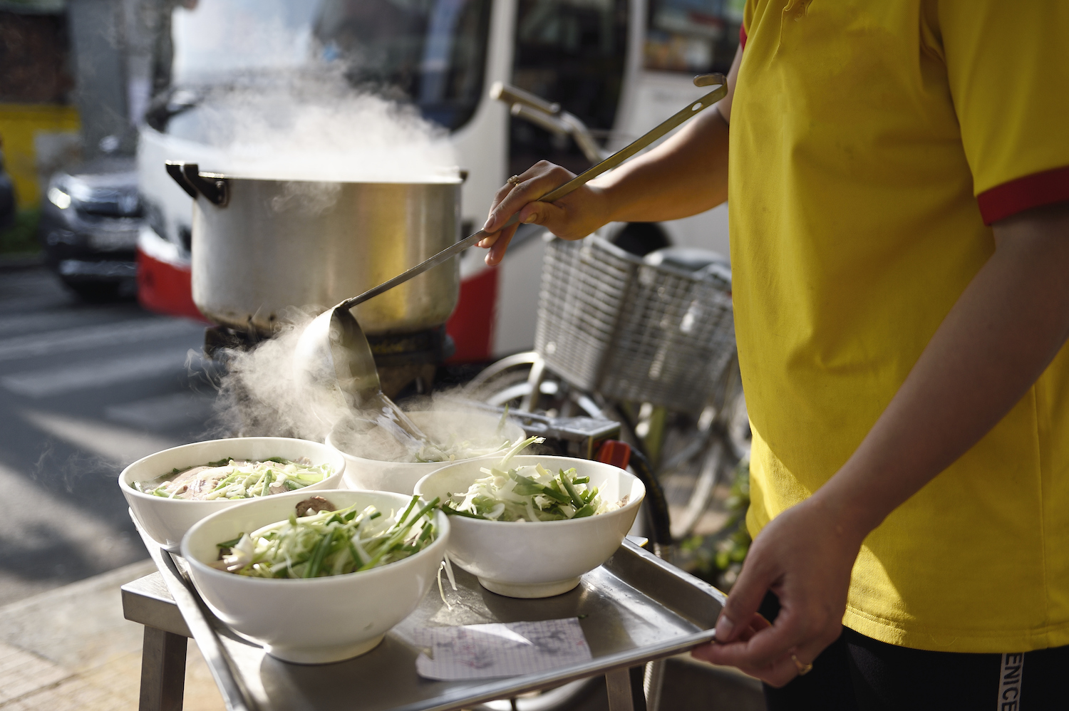 Hands pouring broth into bowls of pho