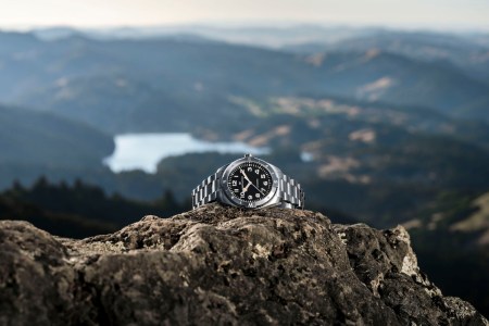 Silver watch on a cliff in front of water landscape