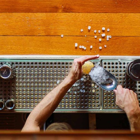 A bartender pouring pebbled ice into a glass on a bar counter. A viral TikTok trend of asking for "less ice" will only hurt your drink.