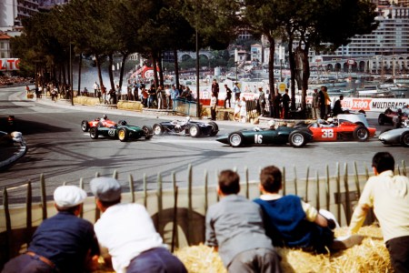 An old-school image of men crouched on a hill, watching racecars.